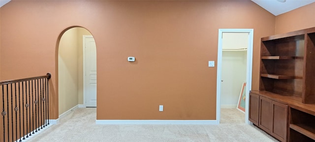 empty room featuring arched walkways, light colored carpet, vaulted ceiling, and baseboards
