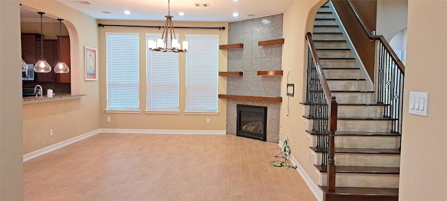 unfurnished living room with recessed lighting, wood finished floors, baseboards, stairs, and a glass covered fireplace