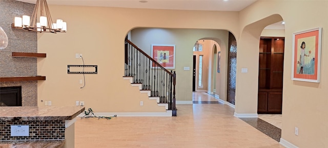 foyer featuring arched walkways, a fireplace, wood finished floors, baseboards, and stairway