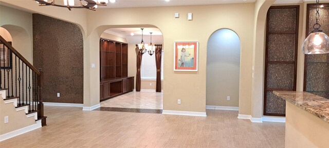foyer with arched walkways, baseboards, light wood-style flooring, stairs, and a chandelier