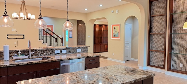 kitchen with decorative light fixtures, a sink, light stone countertops, dark brown cabinets, and stainless steel dishwasher