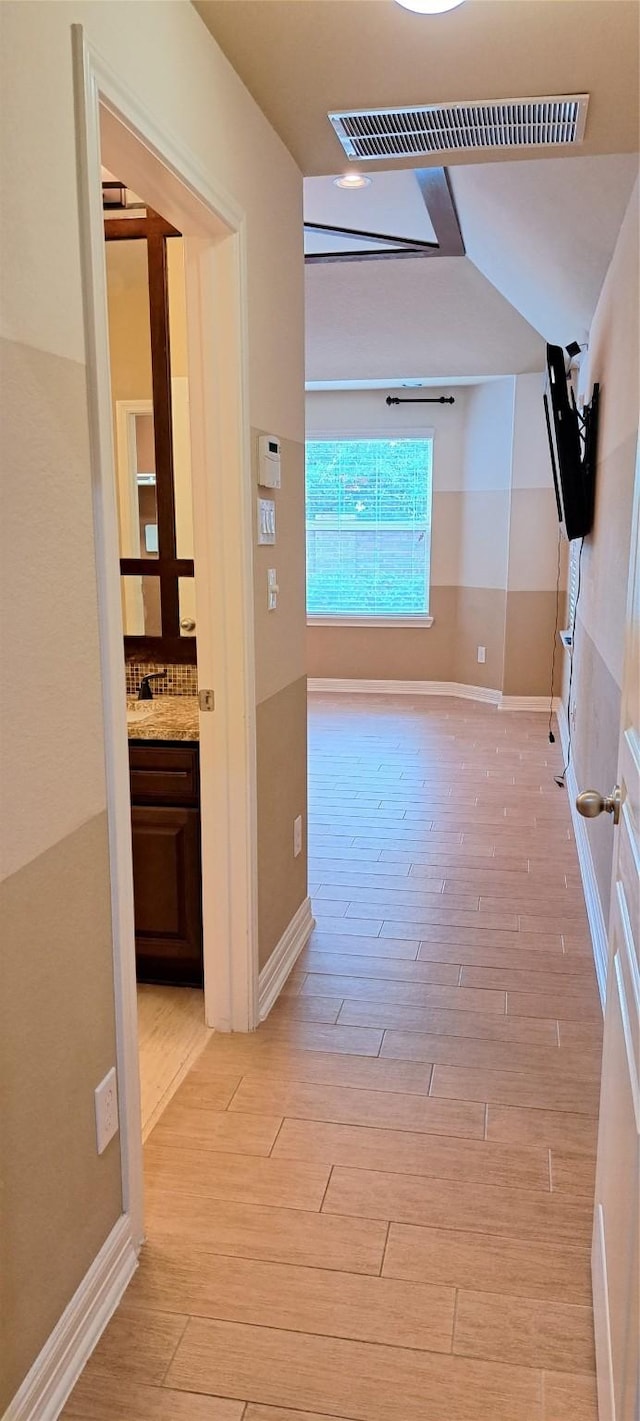 hallway with light wood-style floors, visible vents, and baseboards