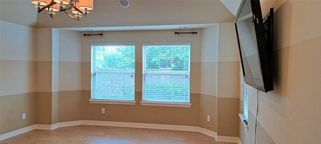 empty room with a chandelier, wood finished floors, and a wealth of natural light