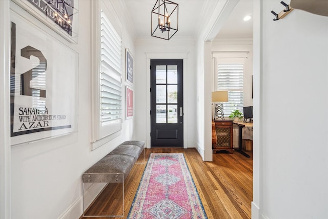 foyer entrance featuring baseboards, a chandelier, crown molding, and wood finished floors