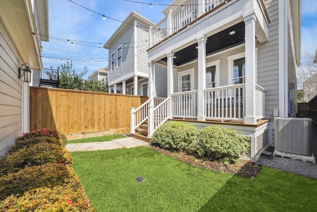 view of yard featuring a balcony, covered porch, fence, and central AC unit