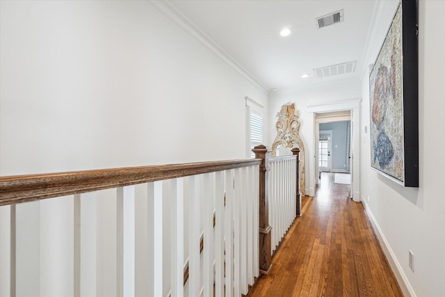 hallway with baseboards, wood finished floors, visible vents, and crown molding