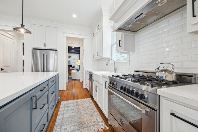 kitchen with premium appliances, dark wood-type flooring, wall chimney range hood, white cabinetry, and backsplash