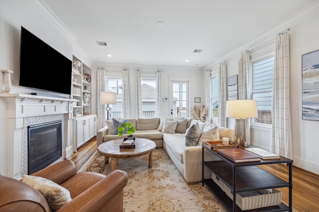 living room featuring light wood-type flooring, a glass covered fireplace, crown molding, and visible vents