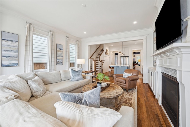 living room featuring crown molding, recessed lighting, stairway, a glass covered fireplace, and wood finished floors