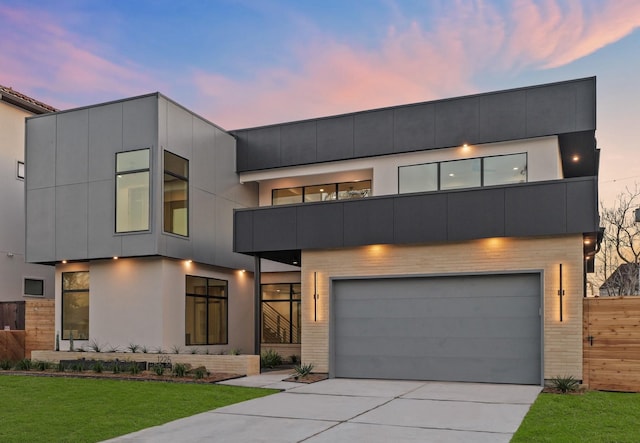 modern home featuring a garage, driveway, a front lawn, and a balcony