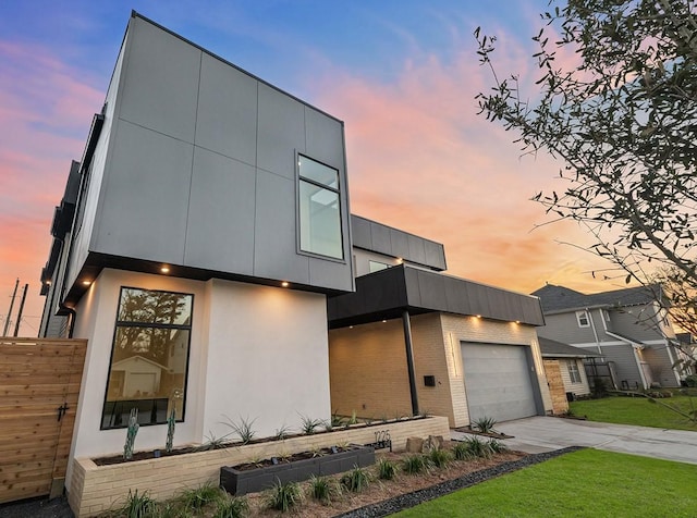 contemporary house featuring an attached garage, brick siding, concrete driveway, stucco siding, and a front yard