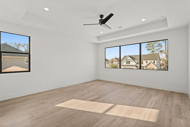 spare room with a wealth of natural light, a tray ceiling, and light wood-style flooring