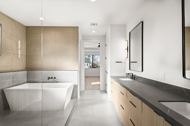 bathroom featuring a sink, visible vents, tile walls, a freestanding bath, and double vanity