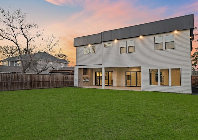 back of house at dusk with a patio area, fence, and a lawn