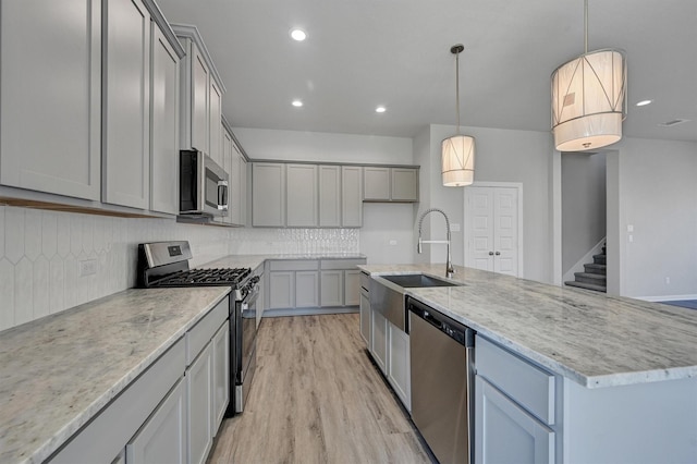 kitchen featuring decorative backsplash, stainless steel appliances, a sink, and gray cabinetry