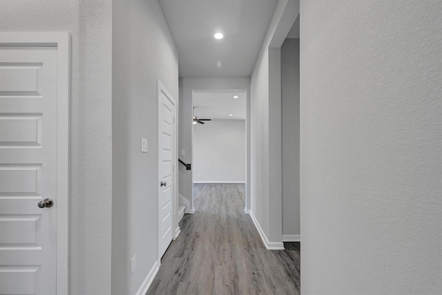 hall with a textured wall, recessed lighting, wood finished floors, and baseboards