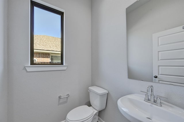 half bath featuring toilet, baseboards, and a sink