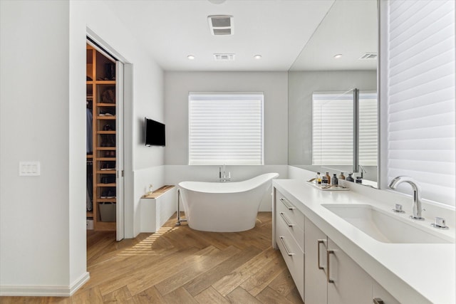 bathroom with a walk in closet, recessed lighting, visible vents, a freestanding bath, and vanity