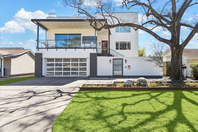 view of front facade with a front yard, concrete driveway, a balcony, and stucco siding