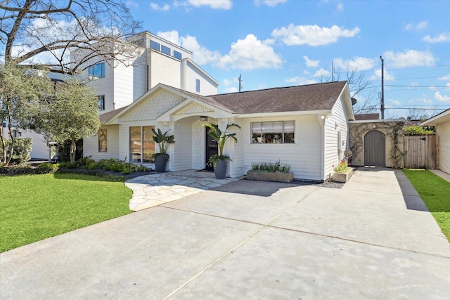 view of front facade featuring a shingled roof, a front yard, and a gate