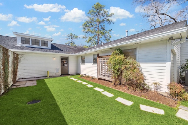 rear view of property with a lawn and roof with shingles