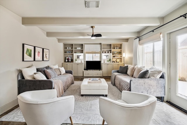 living area featuring a ceiling fan, baseboards, visible vents, and beam ceiling