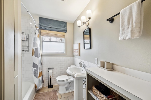 full bath with toilet, a wainscoted wall, shower / tub combo, tile walls, and tile patterned floors