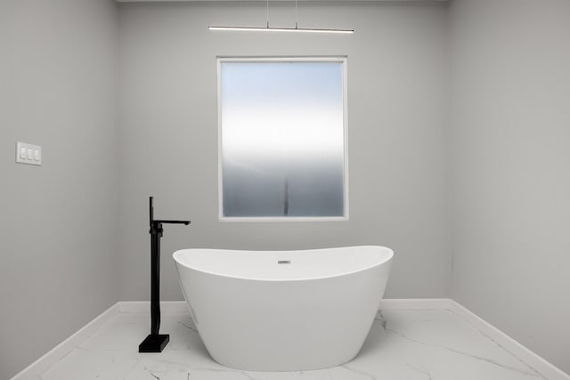 bathroom with marble finish floor, a soaking tub, and baseboards