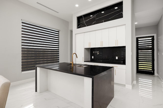 kitchen featuring dark countertops, marble finish floor, white cabinetry, and a sink