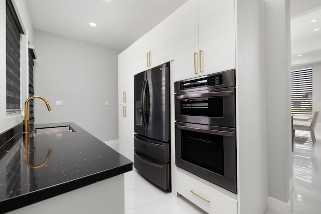 kitchen featuring marble finish floor, double oven, white cabinetry, a sink, and black fridge