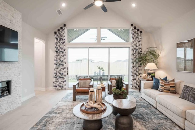 living area with a large fireplace, visible vents, baseboards, ceiling fan, and high vaulted ceiling