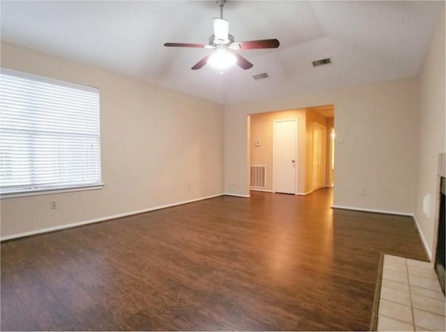 unfurnished room with a ceiling fan, visible vents, wood finished floors, and a tile fireplace