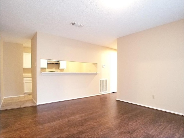 unfurnished living room featuring baseboards, a textured ceiling, visible vents, and wood finished floors