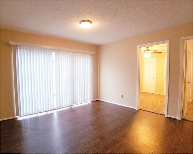 empty room featuring a healthy amount of sunlight, dark wood finished floors, a textured ceiling, and baseboards