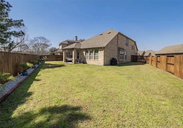 back of house with a lawn, brick siding, and a fenced backyard