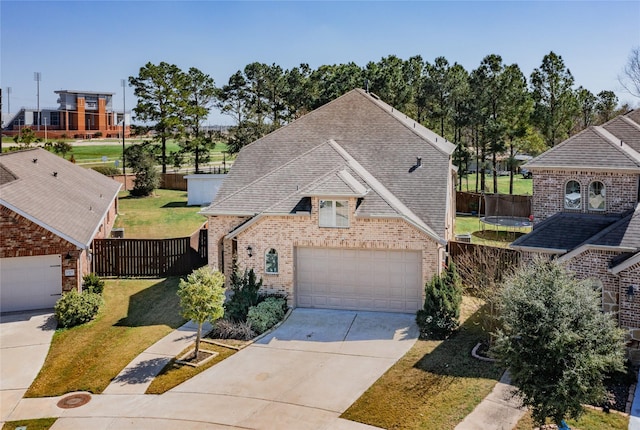 view of front of property featuring a trampoline, fence, roof with shingles, a garage, and brick siding