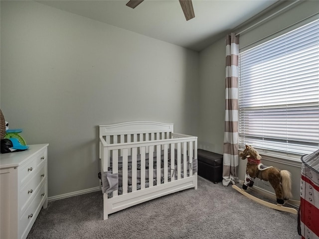 carpeted bedroom featuring a crib, baseboards, and ceiling fan