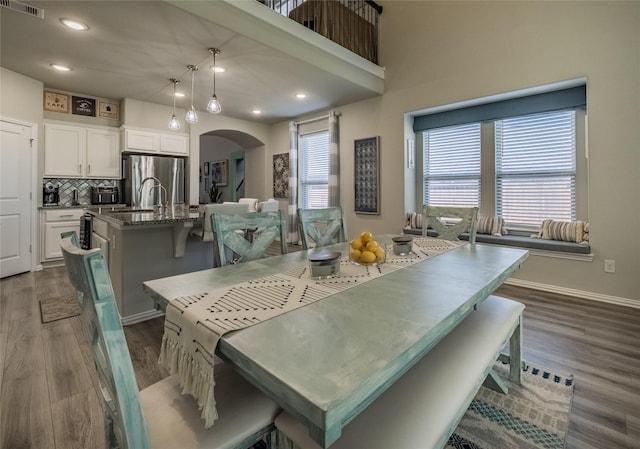 dining space featuring dark wood-style floors, a healthy amount of sunlight, arched walkways, and baseboards