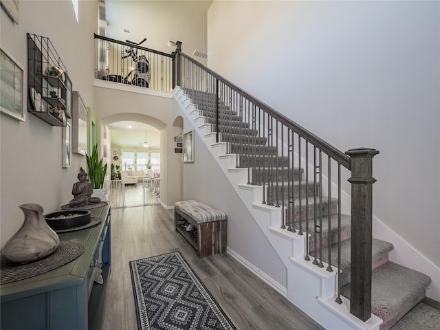 entryway with visible vents, wood finished floors, arched walkways, a high ceiling, and baseboards