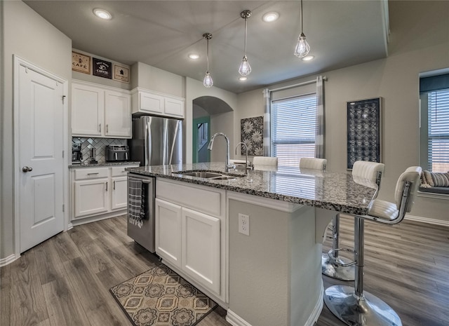 kitchen featuring dark wood finished floors, dark stone countertops, arched walkways, stainless steel appliances, and a sink