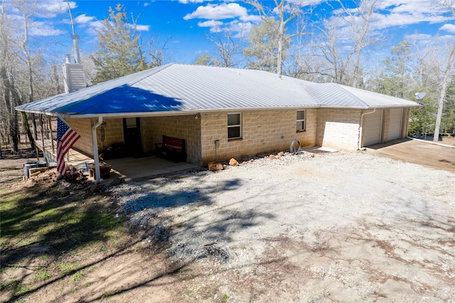 view of property exterior featuring a garage, concrete block siding, driveway, and metal roof