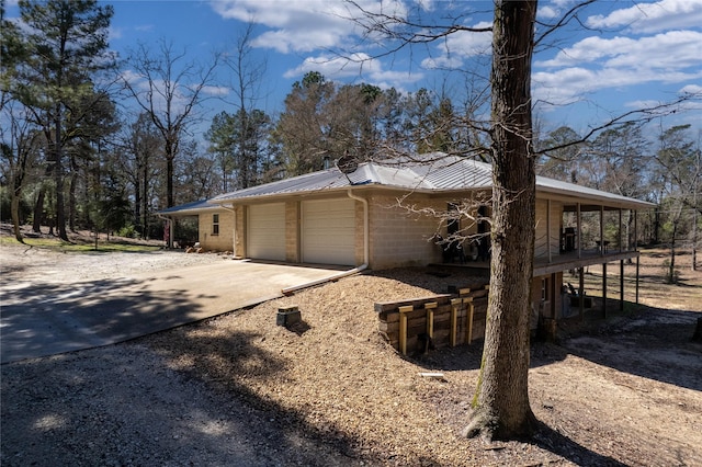 view of property exterior featuring driveway, an attached garage, concrete block siding, and metal roof