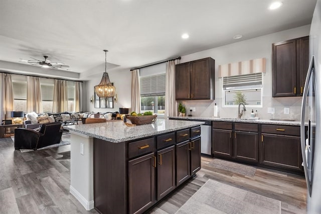 kitchen with light wood finished floors, dark brown cabinets, open floor plan, and a sink