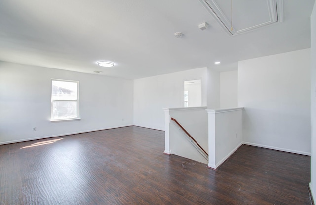 spare room featuring attic access, dark wood-type flooring, and baseboards