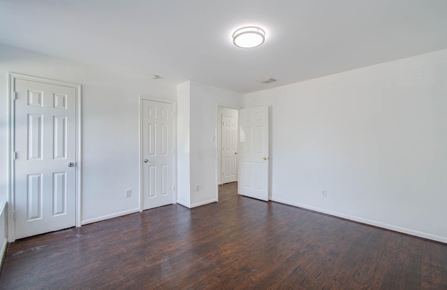 unfurnished bedroom with baseboards, visible vents, and dark wood-type flooring