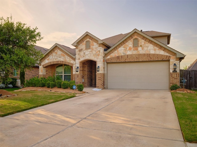 french country home featuring brick siding, concrete driveway, a lawn, an attached garage, and fence