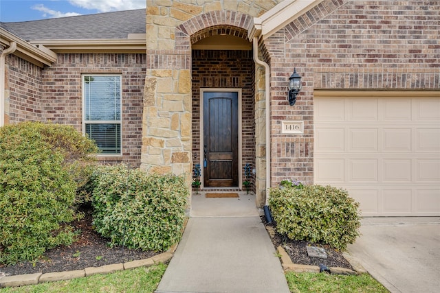 doorway to property with a garage, brick siding, and roof with shingles