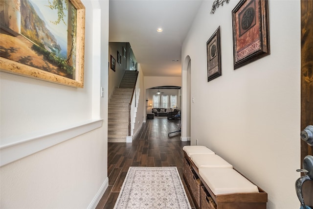 corridor featuring arched walkways, recessed lighting, baseboards, stairs, and dark wood-style floors