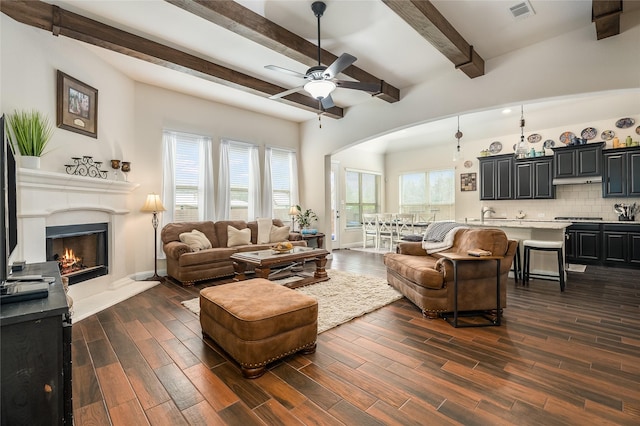 living room with dark wood-style floors, plenty of natural light, a lit fireplace, and a ceiling fan