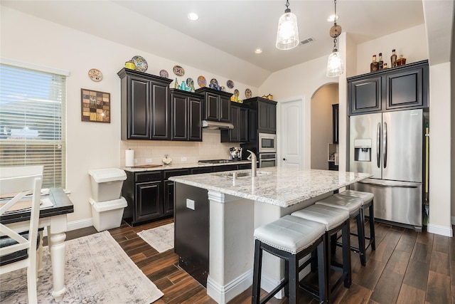 kitchen with arched walkways, stainless steel appliances, tasteful backsplash, a sink, and dark cabinets